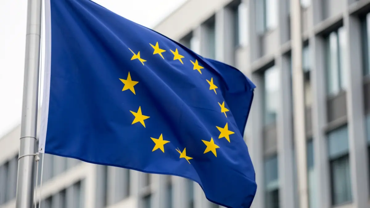 Generic image of a European Union flag gently waving, with the blurred facade of a modern office building in the background.